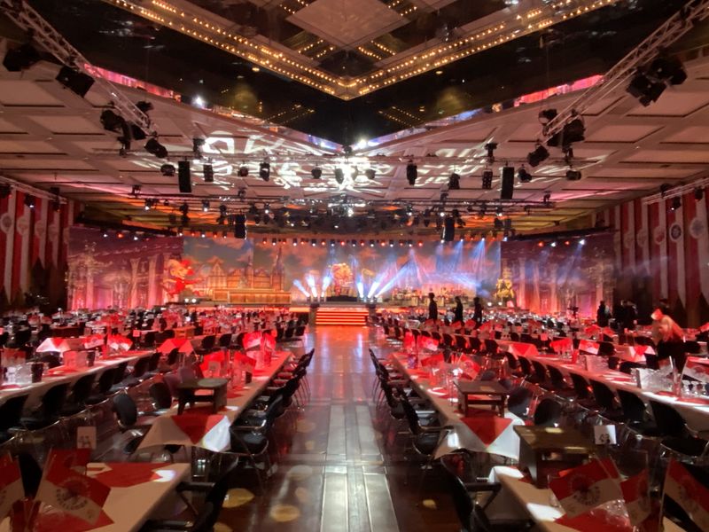 Festlich eingedeckter Gala-Saal mit langen Tafeln, roter Lichtstimmung und Bühne kurz vor dem Einlass