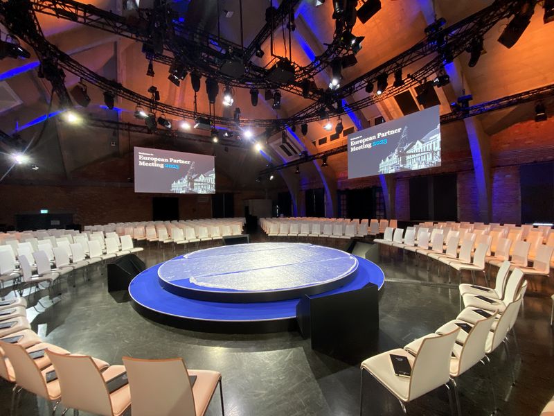 Konferenzaufbau mit runder Bühne, Leinwänden und Bestuhlung in einer historischen Halle